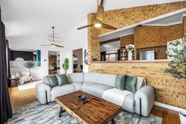 A modern living room with a sectional sofa, a wooden coffee table, and a brick accent wall.