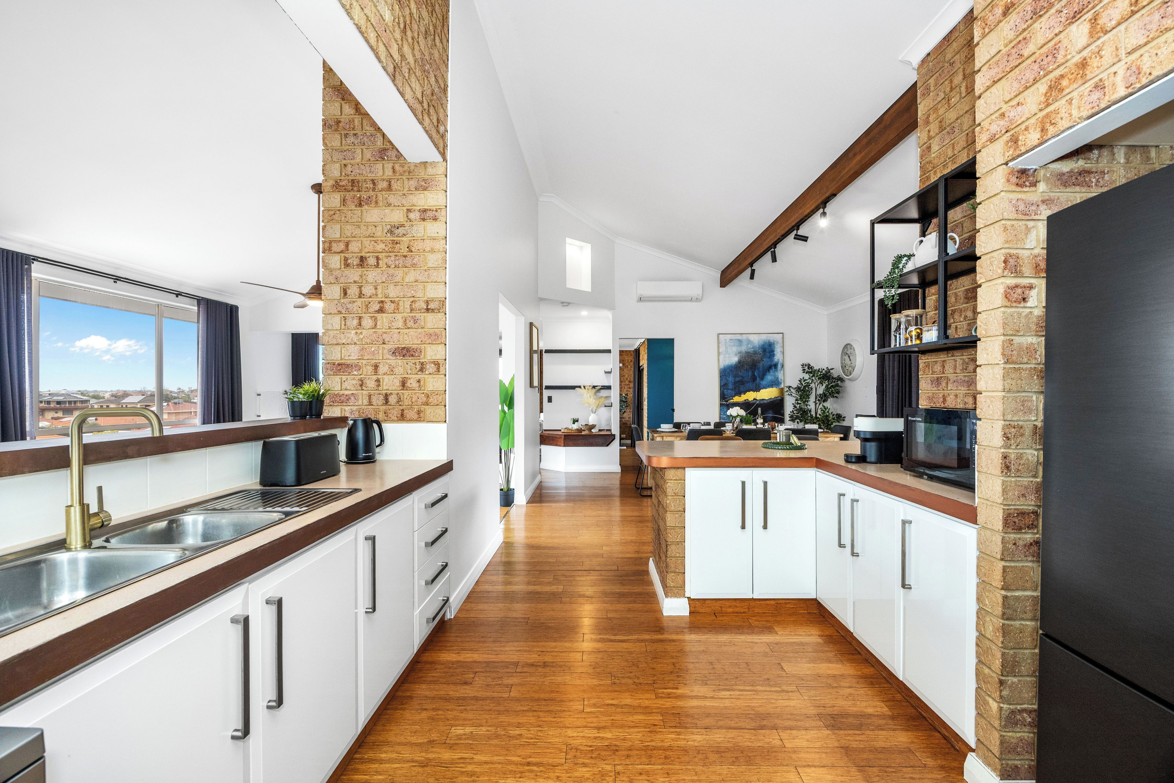 A modern kitchen with white cabinetry, a black refrigerator, and a view of the city through large windows.