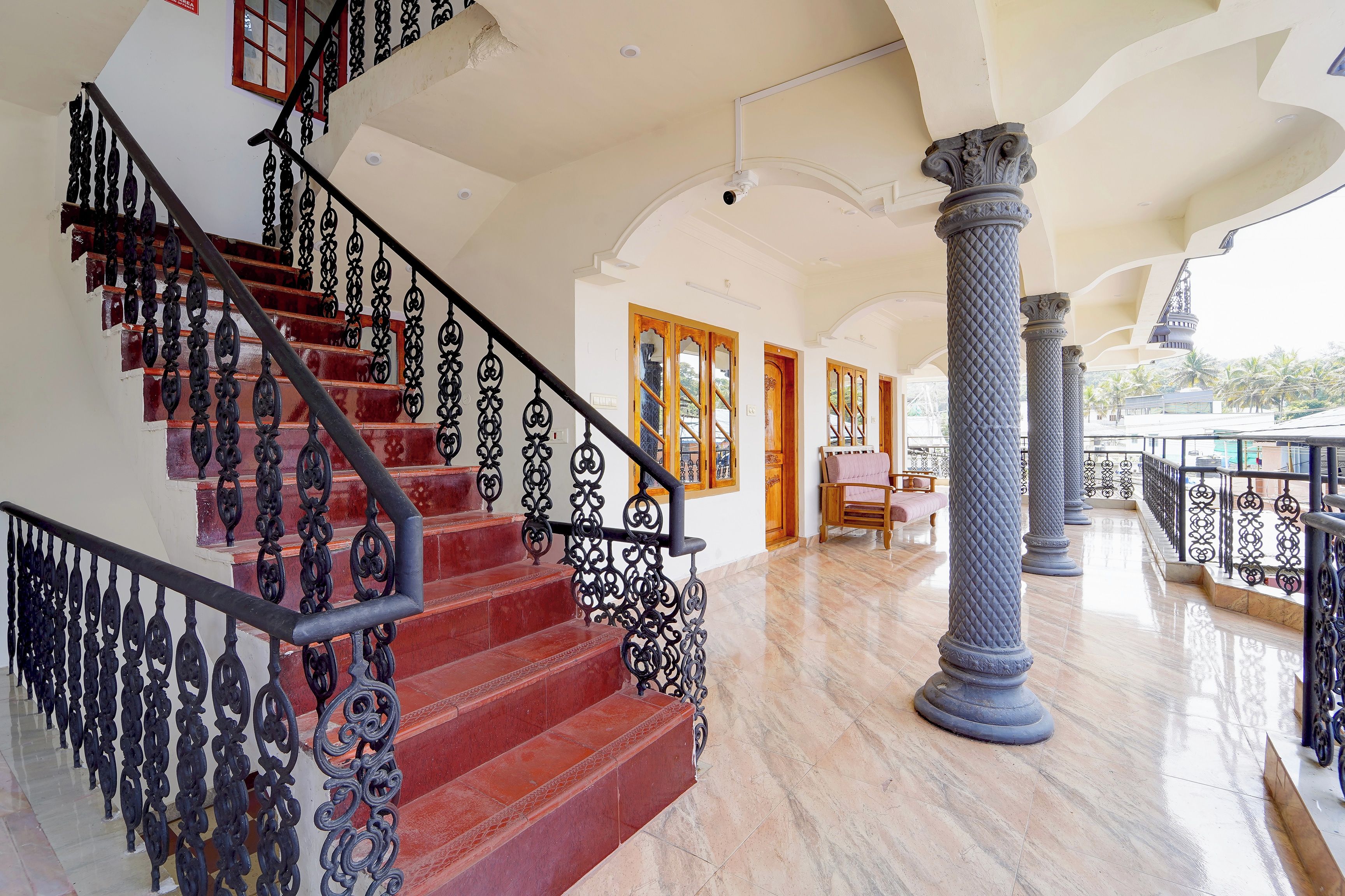 Una majestuosa escalera con barandillas negras ornamentales, que conduce a una habitación con puerta de madera y vistas de palmeras al exterior.
