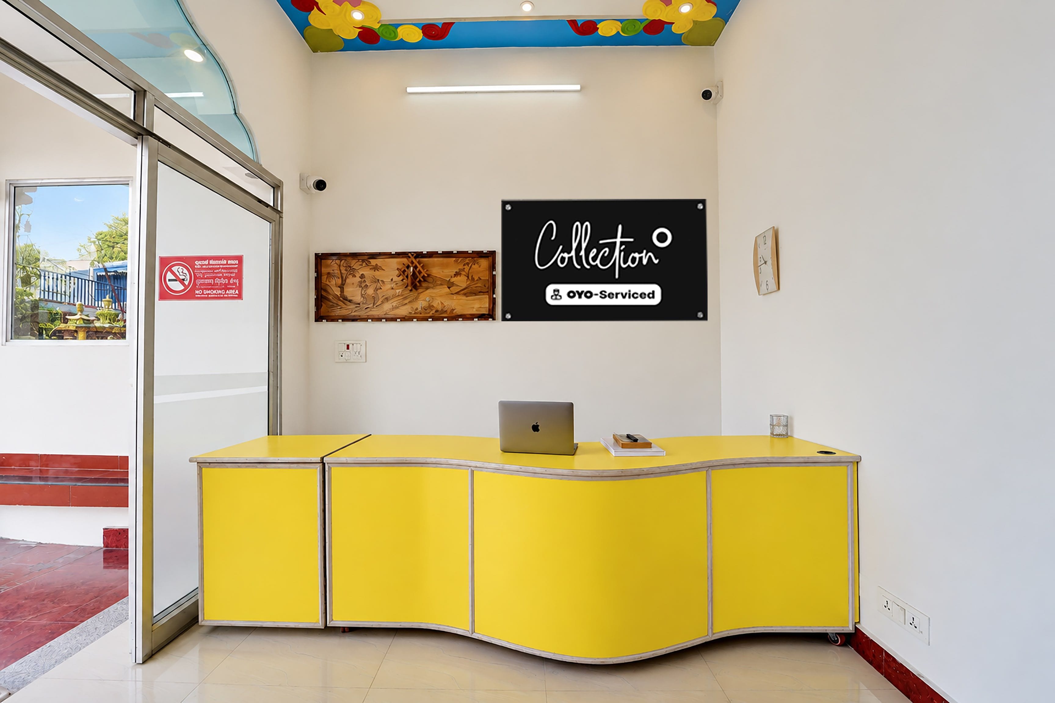 A reception desk with a laptop, a clock, and a sign that reads 'Collection OYO-Serviced'.