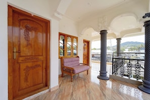 A spacious hallway with a wooden door, a cushioned bench, and a balcony with a metal railing. - Collection O Periyar National Park (Thekkady)