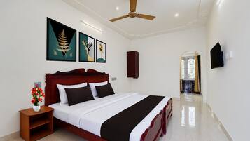 Quarto com cama, mesa de cabeceira, vaso com flores, ventoinha no teto e obras de arte na parede.