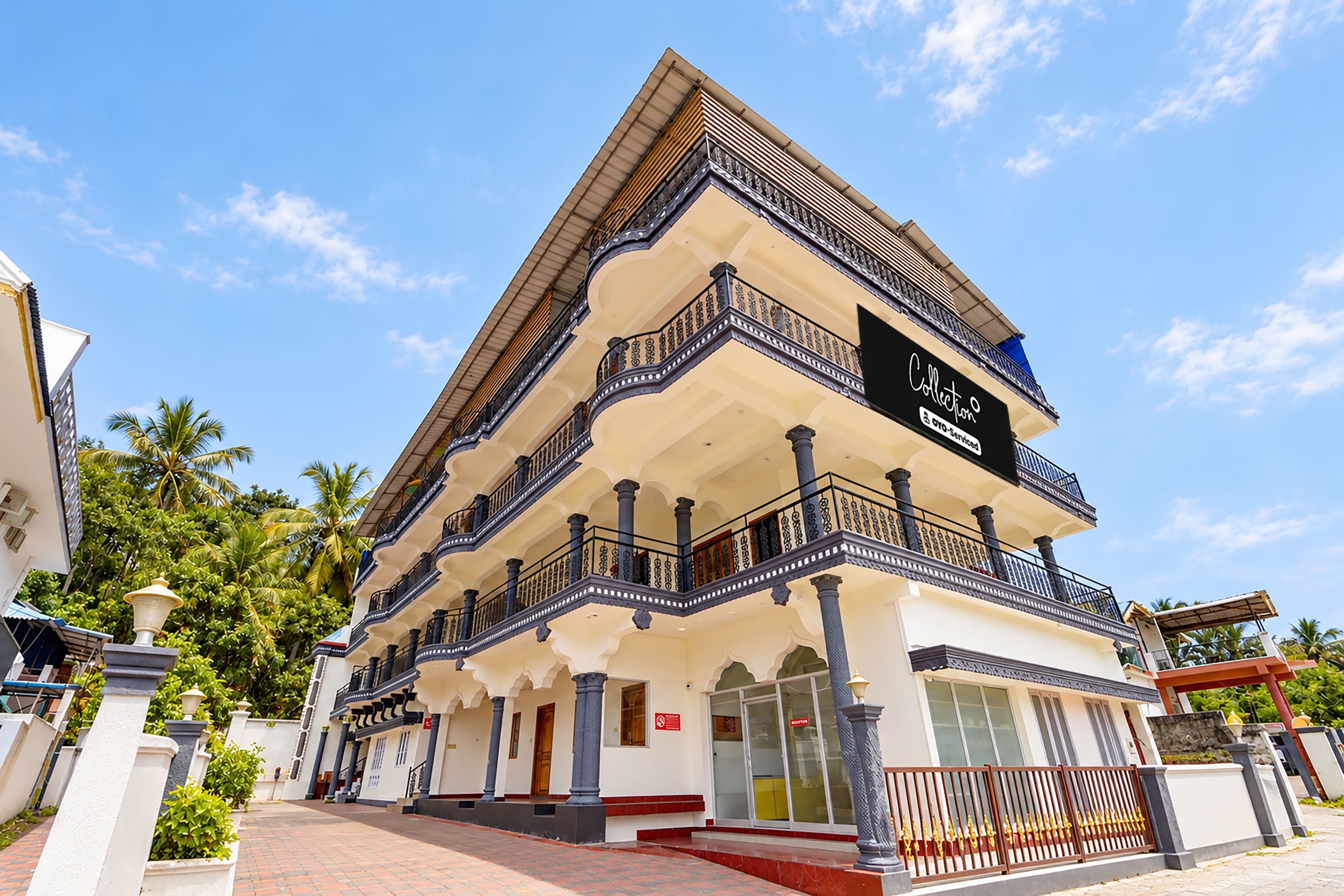 A multi-story hotel with a balcony on the second floor, a sign indicating it is a collection hotel, and a clear sky in the background.
