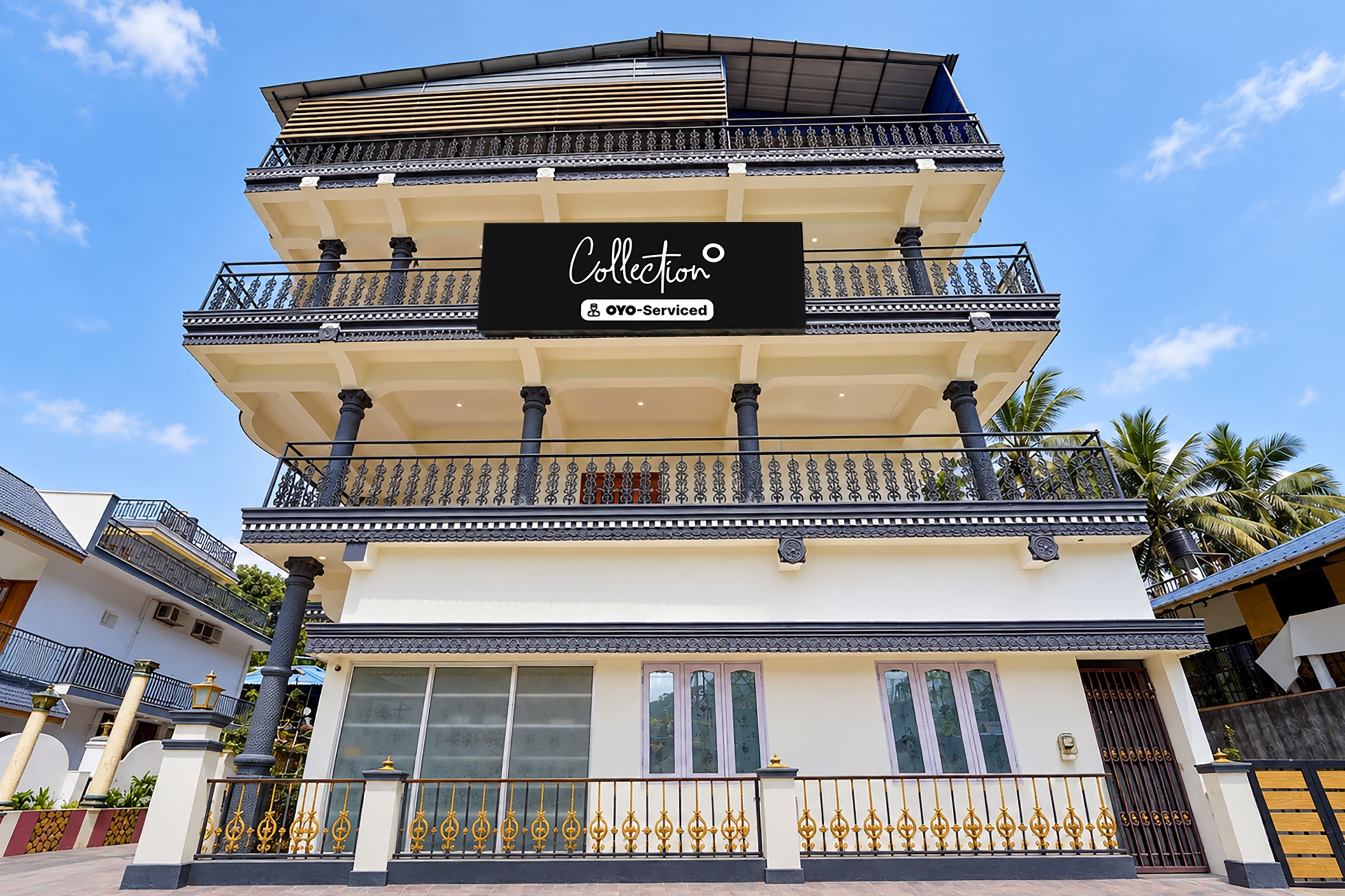A multi-story building with balconies, a sign reading 'Collection OYO-Serviced', and a clear blue sky in the background.