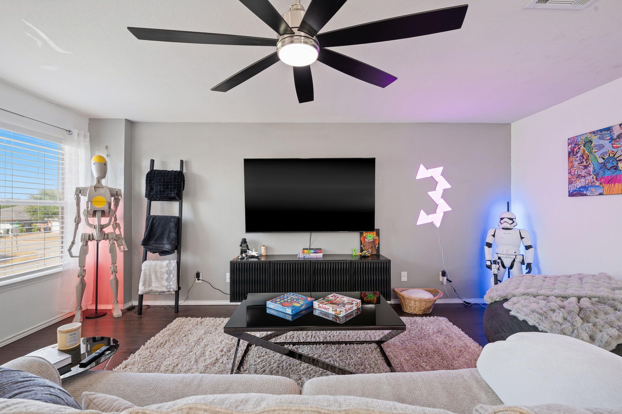 A modern living room with a ceiling fan, a flat-screen TV, and a Star Wars-themed wall decoration.