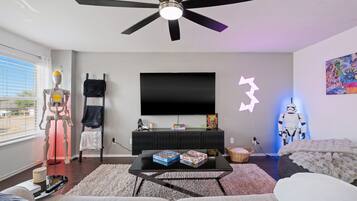 A modern living room with a ceiling fan, a flat-screen TV, and a Star Wars-themed wall decoration.