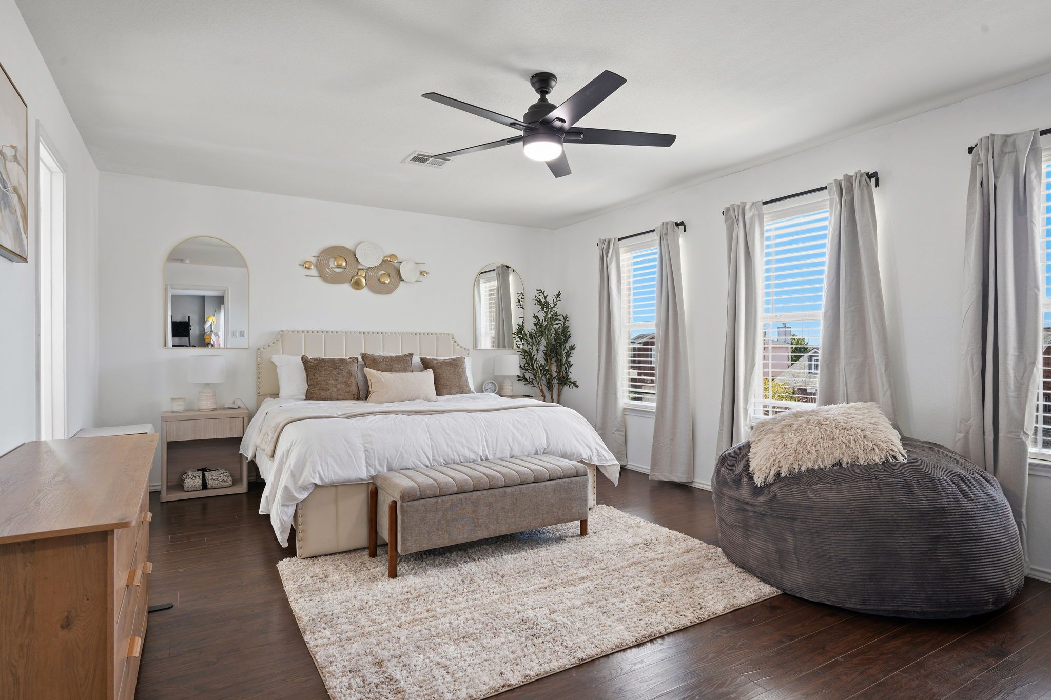 A bedroom with a bed, bedside table, lamp, ceiling fan, and a large window with curtains.