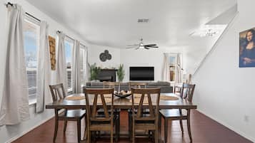 Zona pranzo con tavolo e sedie in legno, televisione a schermo piatto e ventilatore a soffitto.