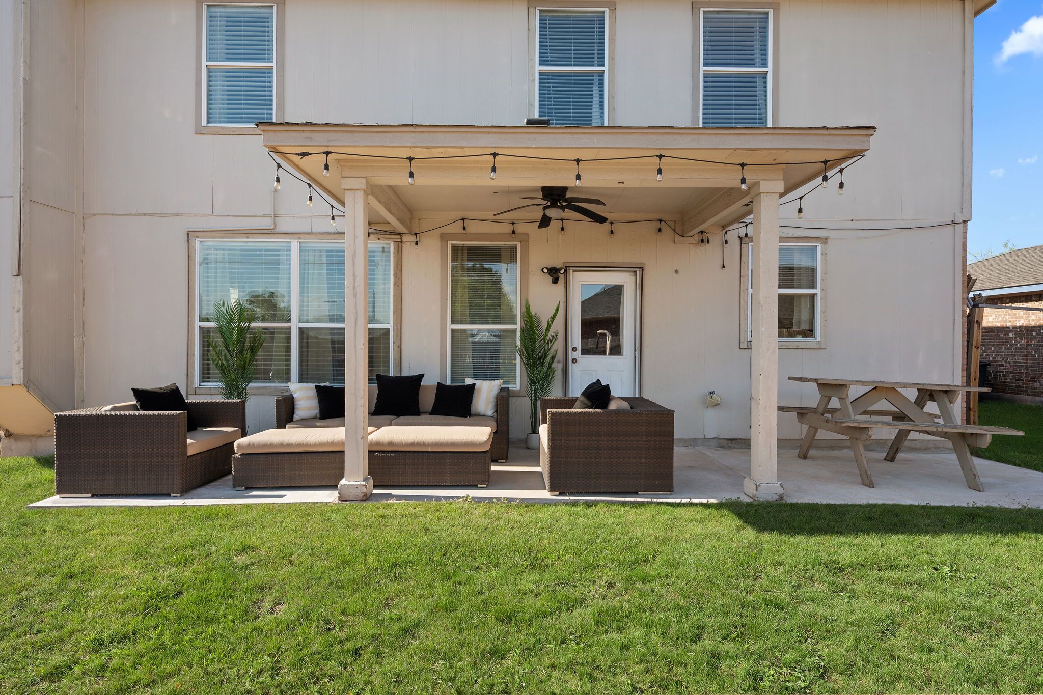 A covered patio area with outdoor furniture, a ceiling fan, and a wooden table.