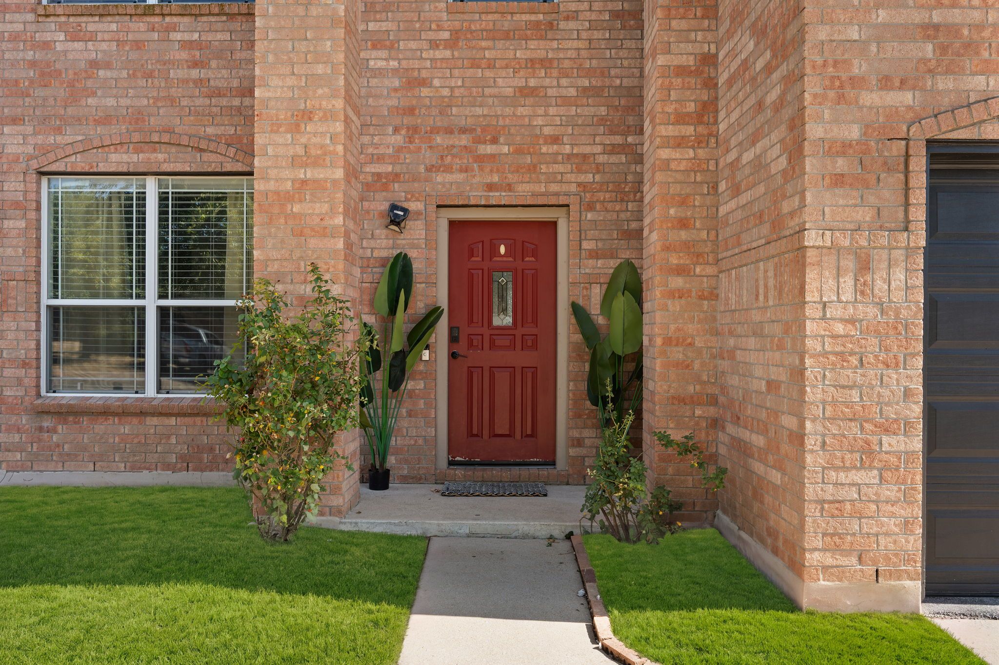 A brick building with a red door, a window, and two potted plants.