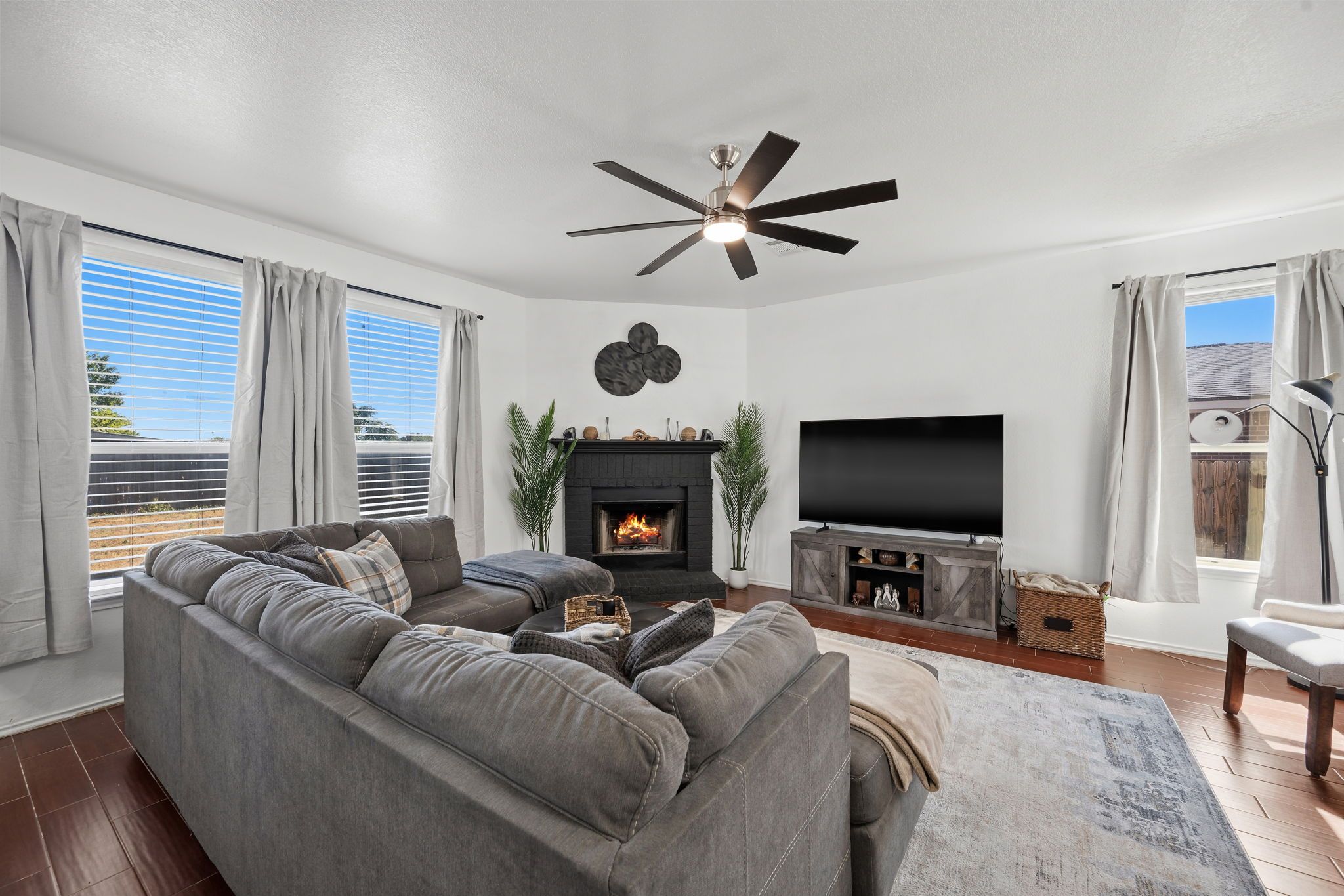 A modern living room with a sectional sofa, a fireplace, a flat-screen TV, and a ceiling fan.