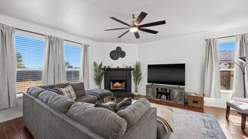 A modern living room with a sectional sofa, a fireplace, a flat-screen TV, and a ceiling fan.
