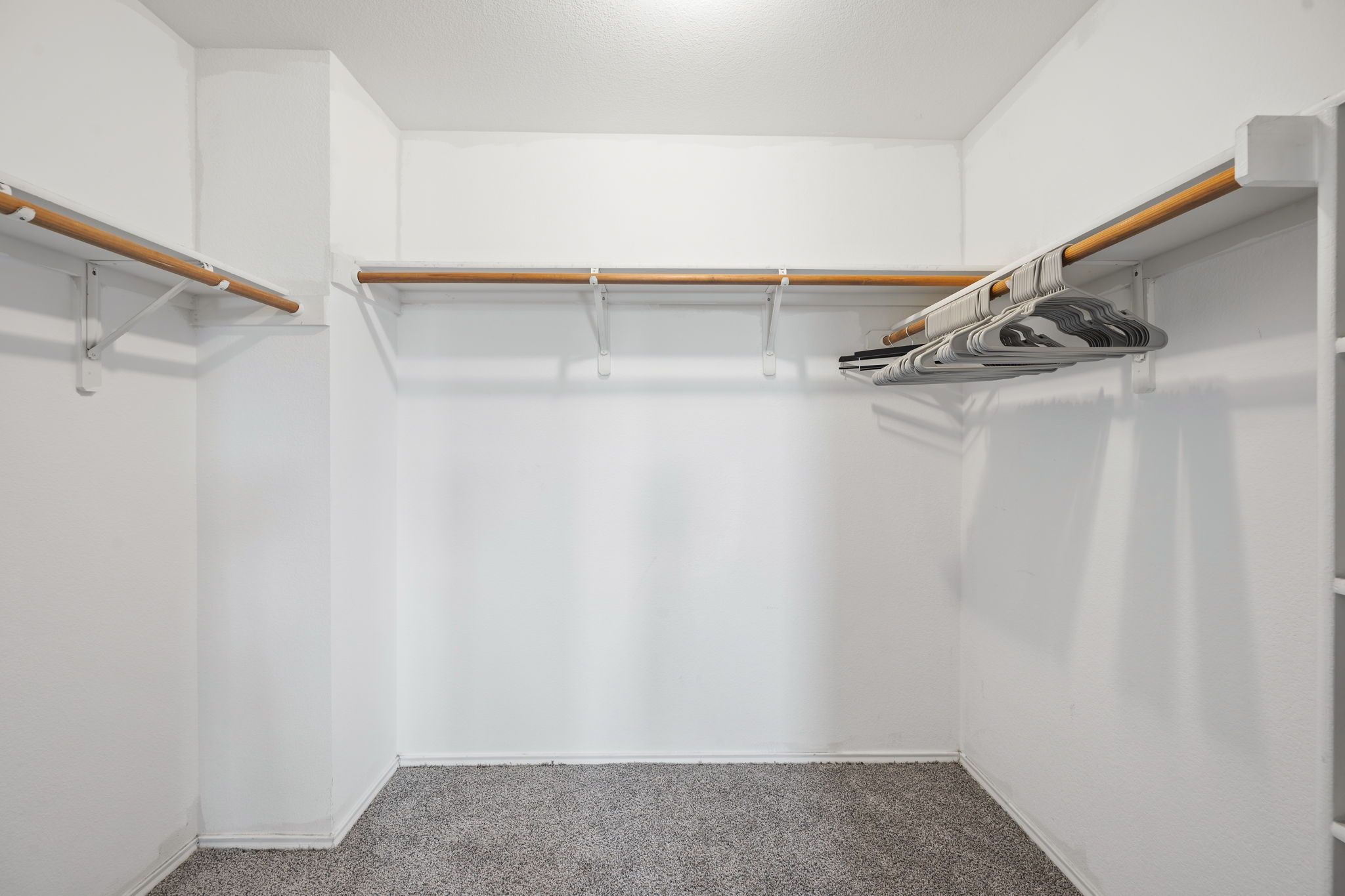 A corner closet with a wooden rod and a metal rack for hanging items.