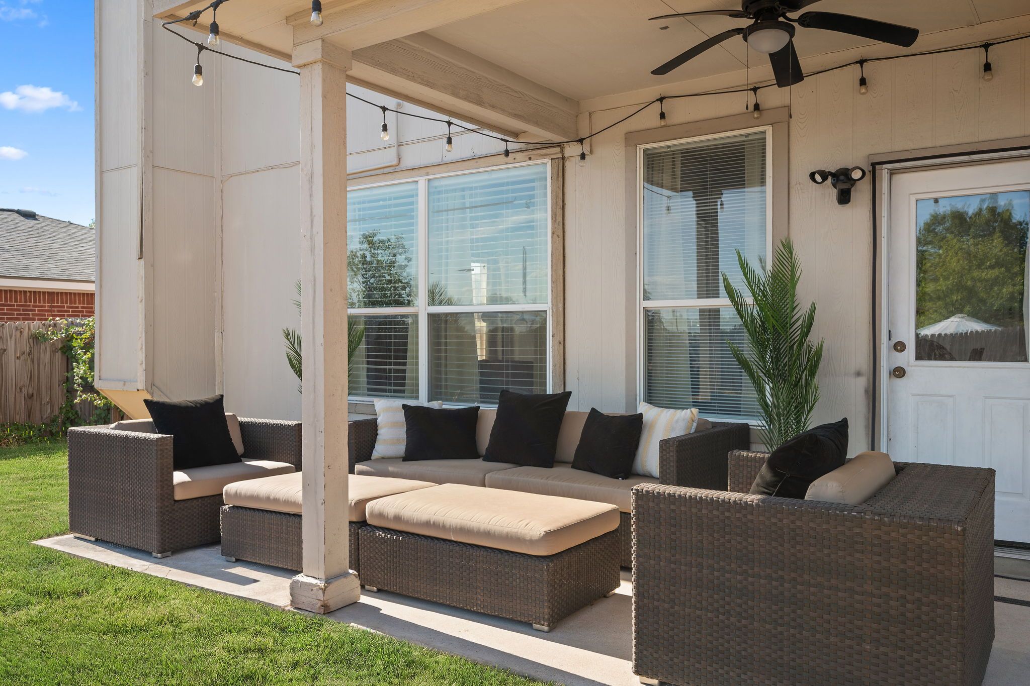 Une terrasse couverte, aménagée avec des meubles en osier et dotée d’un ventilateur de plafond.