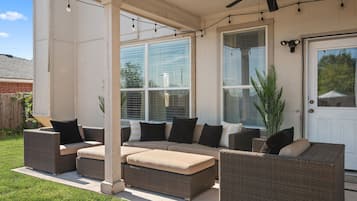 Une terrasse couverte, aménagée avec des meubles en osier et dotée d’un ventilateur de plafond.