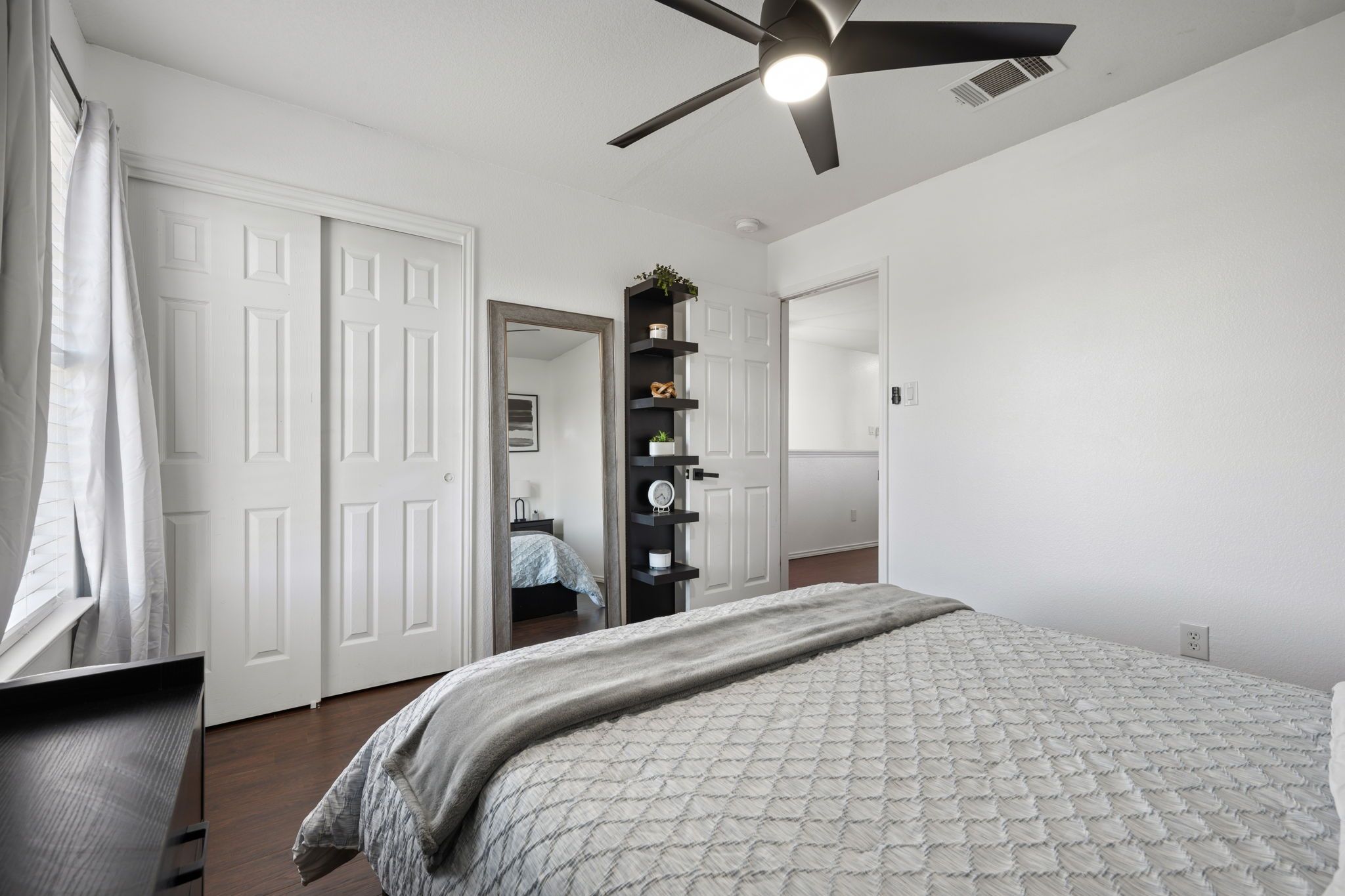 Une chambre à coucher avec un lit, un ventilateur de plafond, une armoire et un miroir.