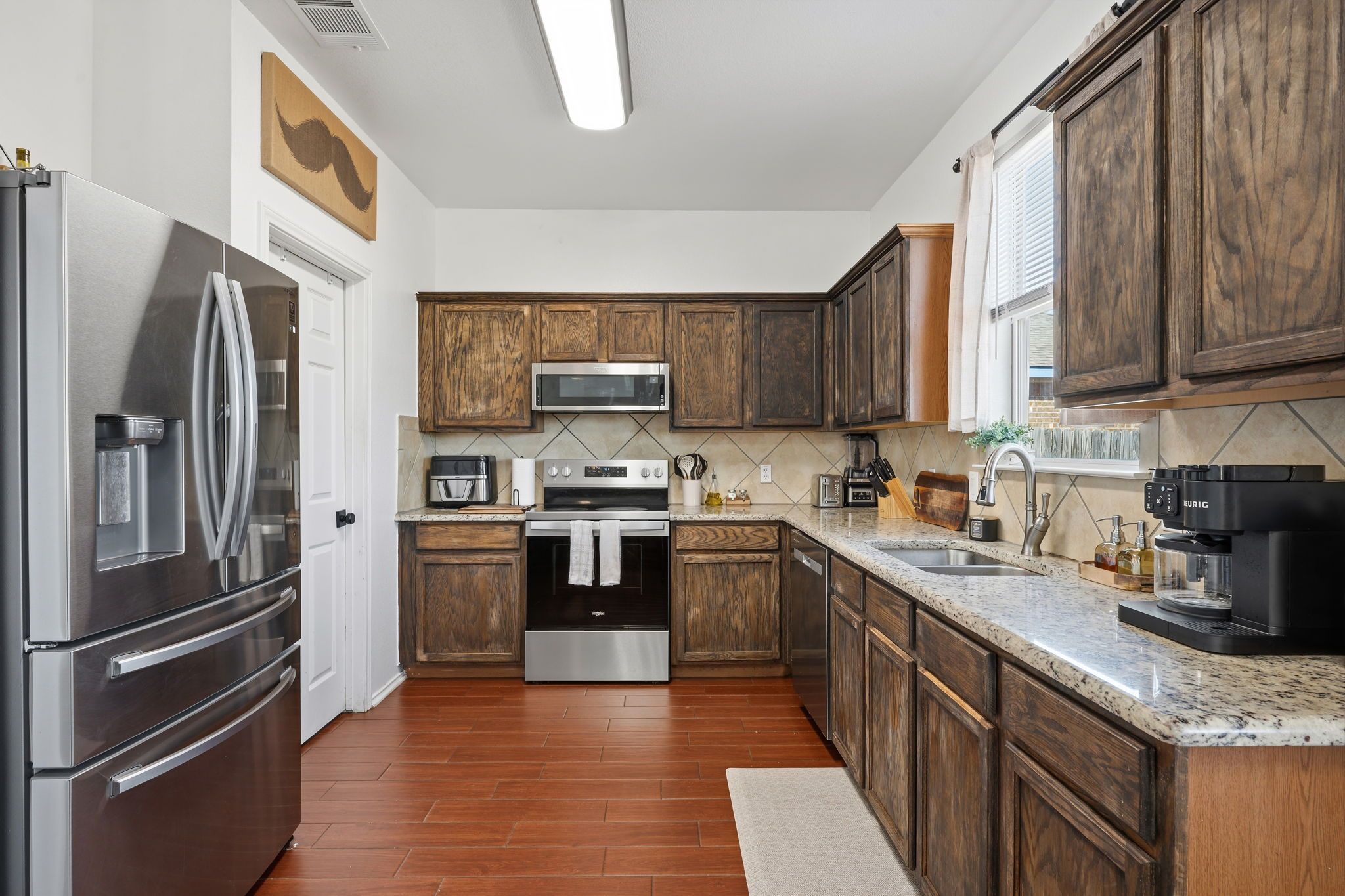 A modern kitchen with wooden cabinets, stainless steel appliances, and a granite countertop.