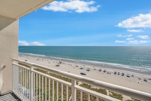 Ein Balkon mit Blick auf einen Strand, einem Geländer und einem klaren Himmel.