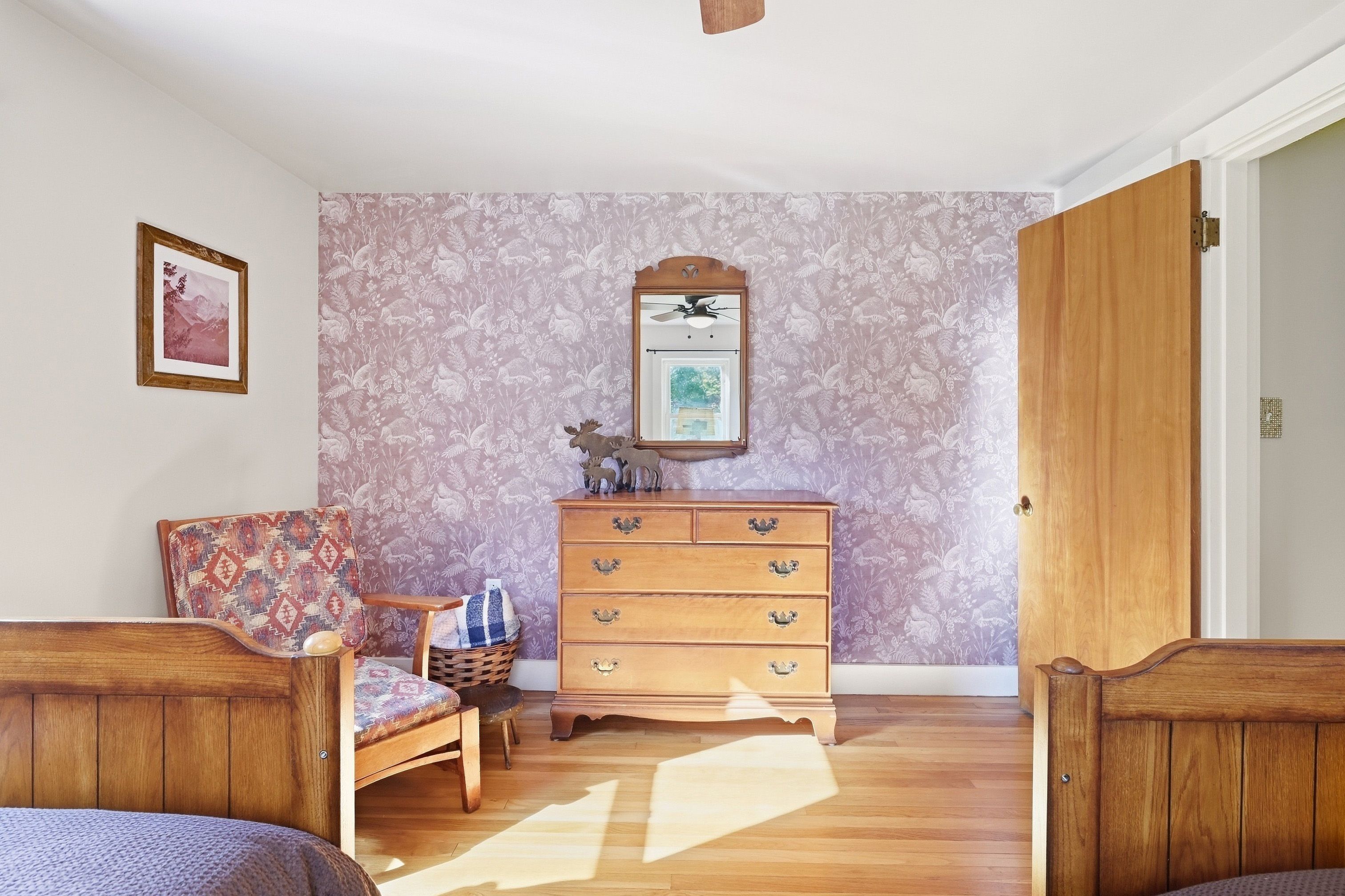 Una habitación con un aparador de madera, una silla con cojín estampado, un cuadro en la pared y una puerta.