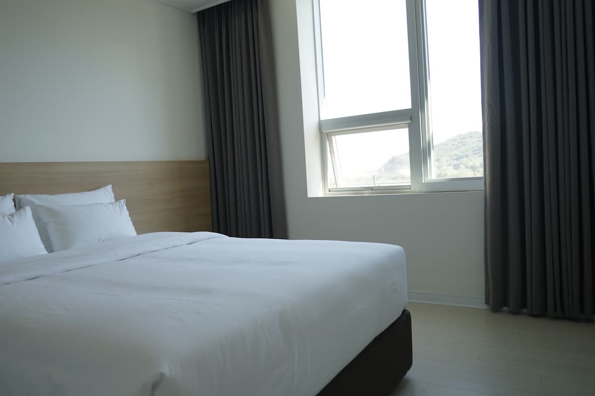 A hotel room with a large bed, a wooden headboard, and a window with curtains.