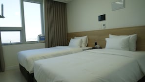A hotel room with two beds, a window with curtains, a bedside table with a bottle, a digital thermostat, and a small screen on the wall. - remainzhotel (Incheon)