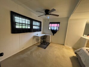 A bedroom with a white desk, a chair, a bed, a ceiling fan, and two windows with black curtains. - Private 2-bedroom house in Bloomington (Bloomington)