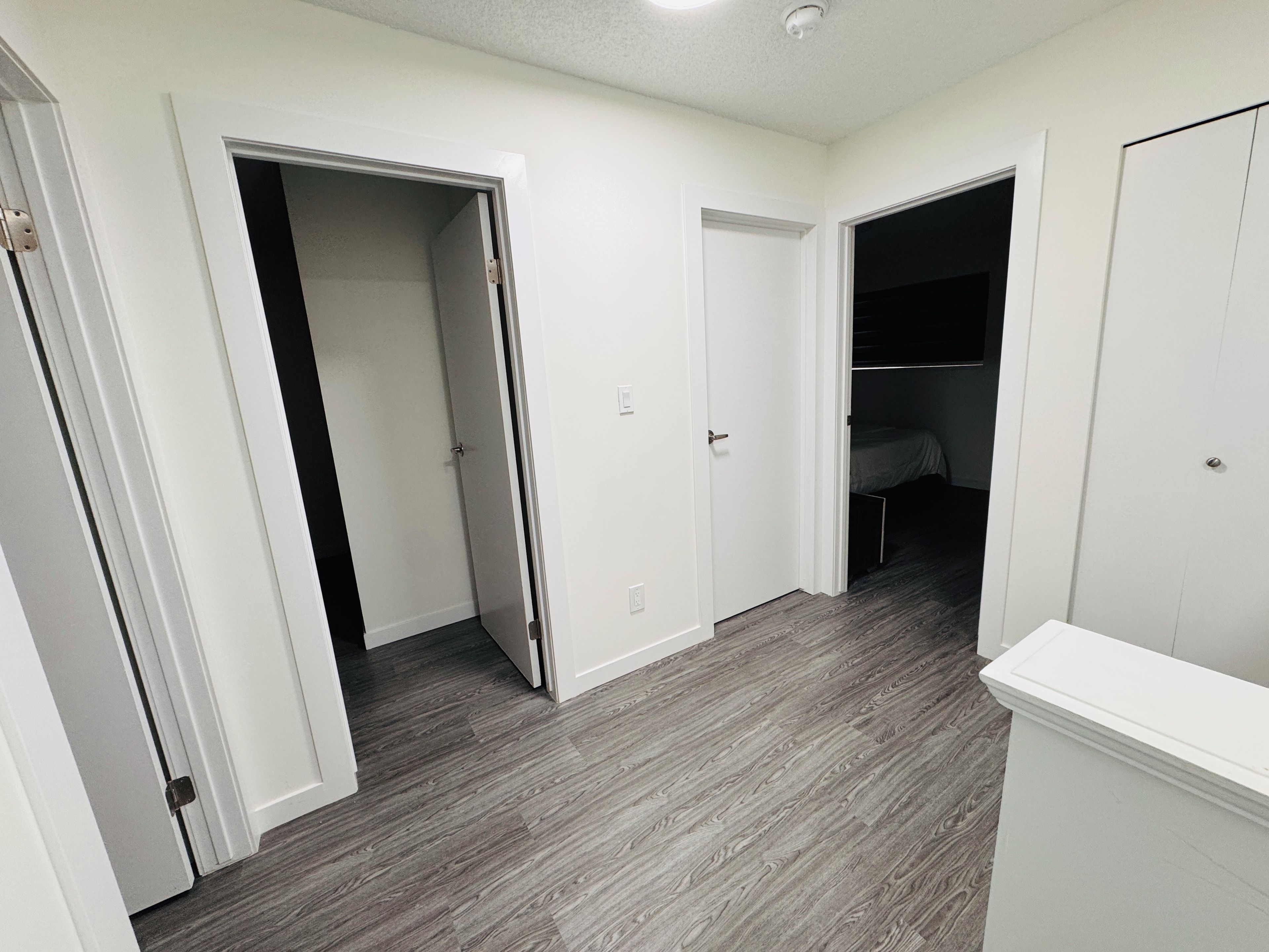A hallway with white doors leading to bedrooms, a ceiling light, and a wooden floor.
