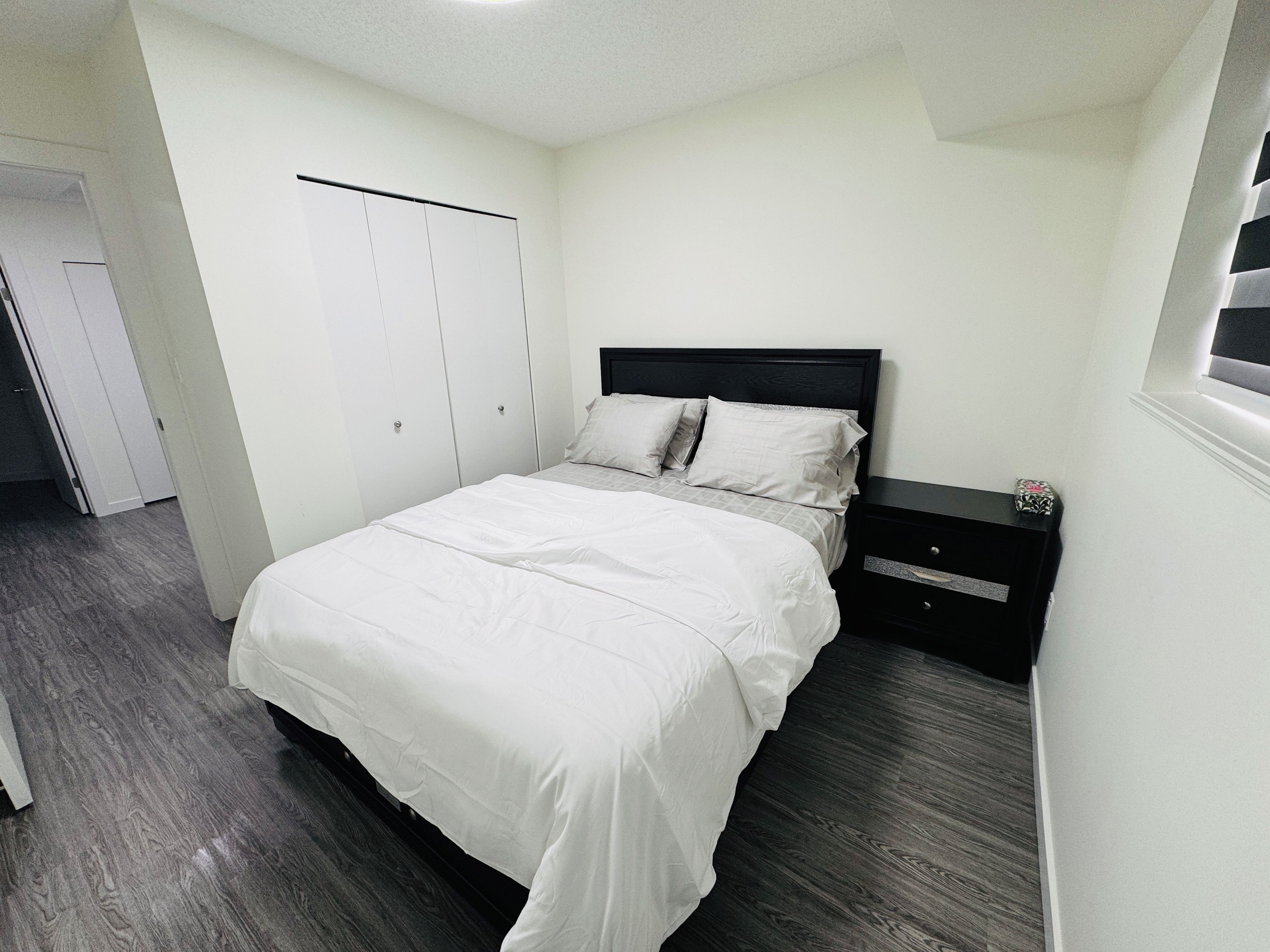 A bedroom with a bed, a nightstand, a wardrobe, and a door.