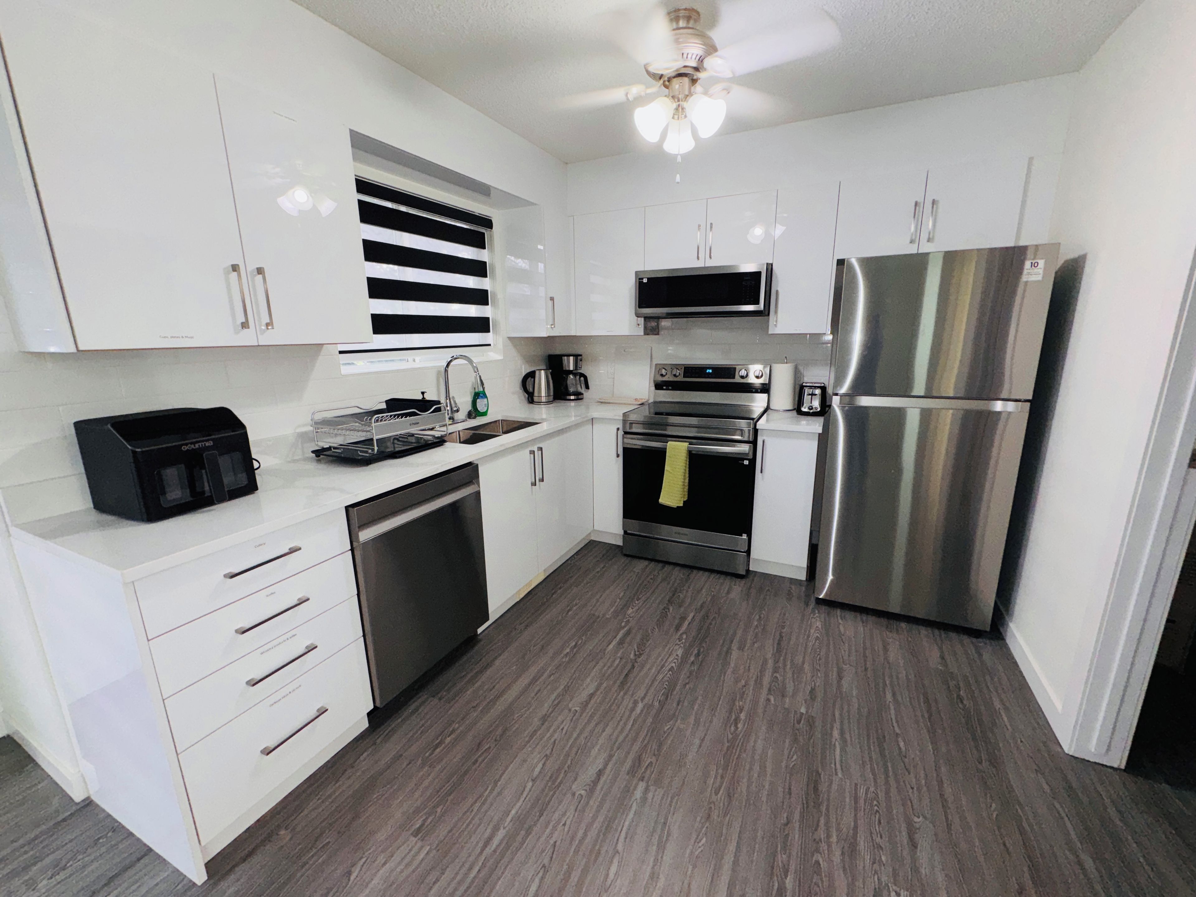 A modern kitchen with white cabinets, stainless steel appliances, and a wooden floor.