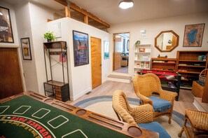 Ein Zimmer mit Billardtisch, Korbmöbeln, einem Bücherregal und einem Poster an der Wand.