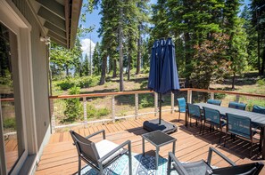 Eine Holzterrasse mit Gartenmöbeln, darunter ein Tisch und Stühle, und einem blauen Sonnenschirm.