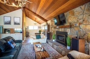 A spacious living area with a stone fireplace, leather sofas, a coffee table, and a television mounted on a stone wall. - Charming 5-bedroom house in South Lake Tahoe perfect for families (South Lake Tahoe)