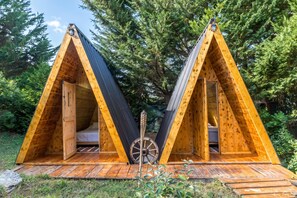 Two wooden A-frame cabins with open doors, a wheelbarrow, and a wooden deck. - Paradise Forest Glamping near Koper Hut 4, Koper, Slovenia (Koper)