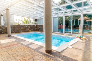 A swimming pool with a tiled border, a stone wall, and a glass-enclosed area with a view of the outdoors. - Paradise Forest Glamping near Koper Hut 4, Koper, Slovenia (Koper)