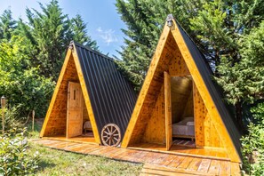 Two wooden A-frame cabins with a wheel chair in front, surrounded by greenery. - Paradise Forest Glamping near Koper Hut 3, Koper, Slovenia (Koper)