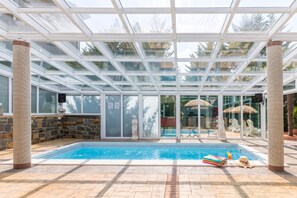 An indoor swimming pool with a glass ceiling, stone pillars, and a view of the outside. - Paradise Forest Glamping near Koper Hut 3, Koper, Slovenia (Koper)