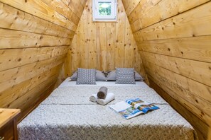 A small, wooden room with a sloped ceiling, a bed with two patterned pillows, a rolled towel, and a magazine on the bed. - Paradise Forest Glamping near Koper Hut 3, Koper, Slovenia (Koper)