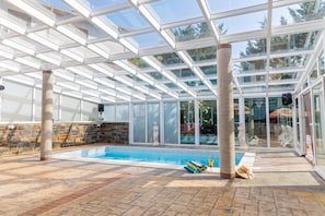 Ein von Glaswänden umgebener Swimmingpool mit Steinmauern und Fliesenboden, unter einer Glaskuppel.