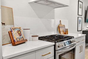 Una cucina moderna con piano cottura a gas, forno, mobili bianchi e un cartello decorativo.