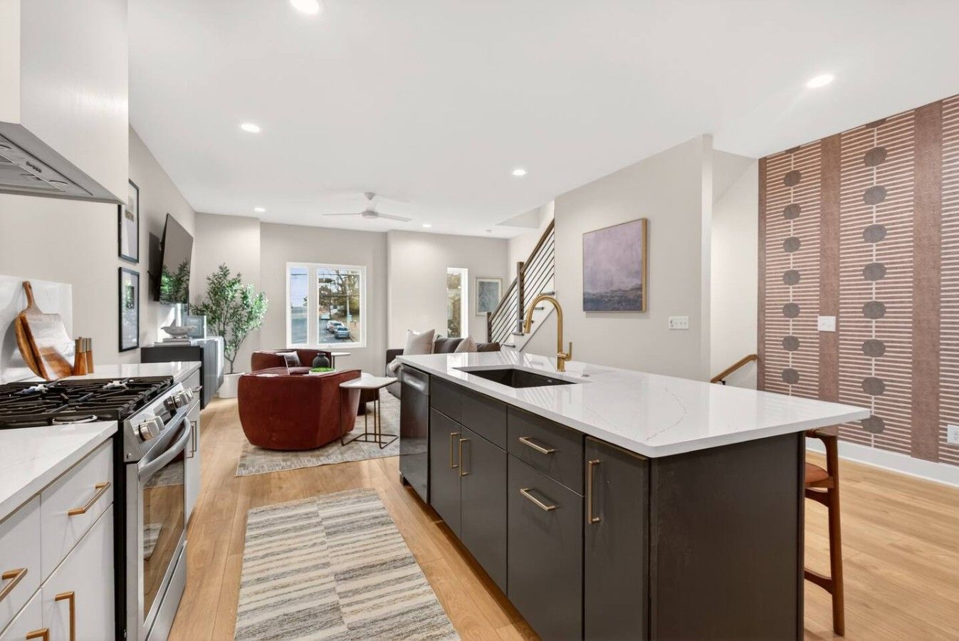 A modern kitchen with a central island, a dining area with a red sofa, and a staircase leading to another level.