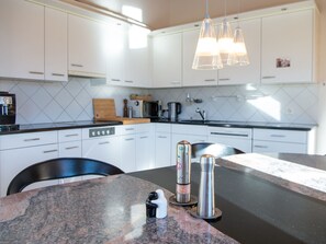 Une cuisine moderne avec des meubles blancs, un plan de travail en granit et une chaise noire.