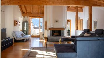 A spacious living room with a fireplace, a sofa, a television, and a large window offering a view of the outdoors.