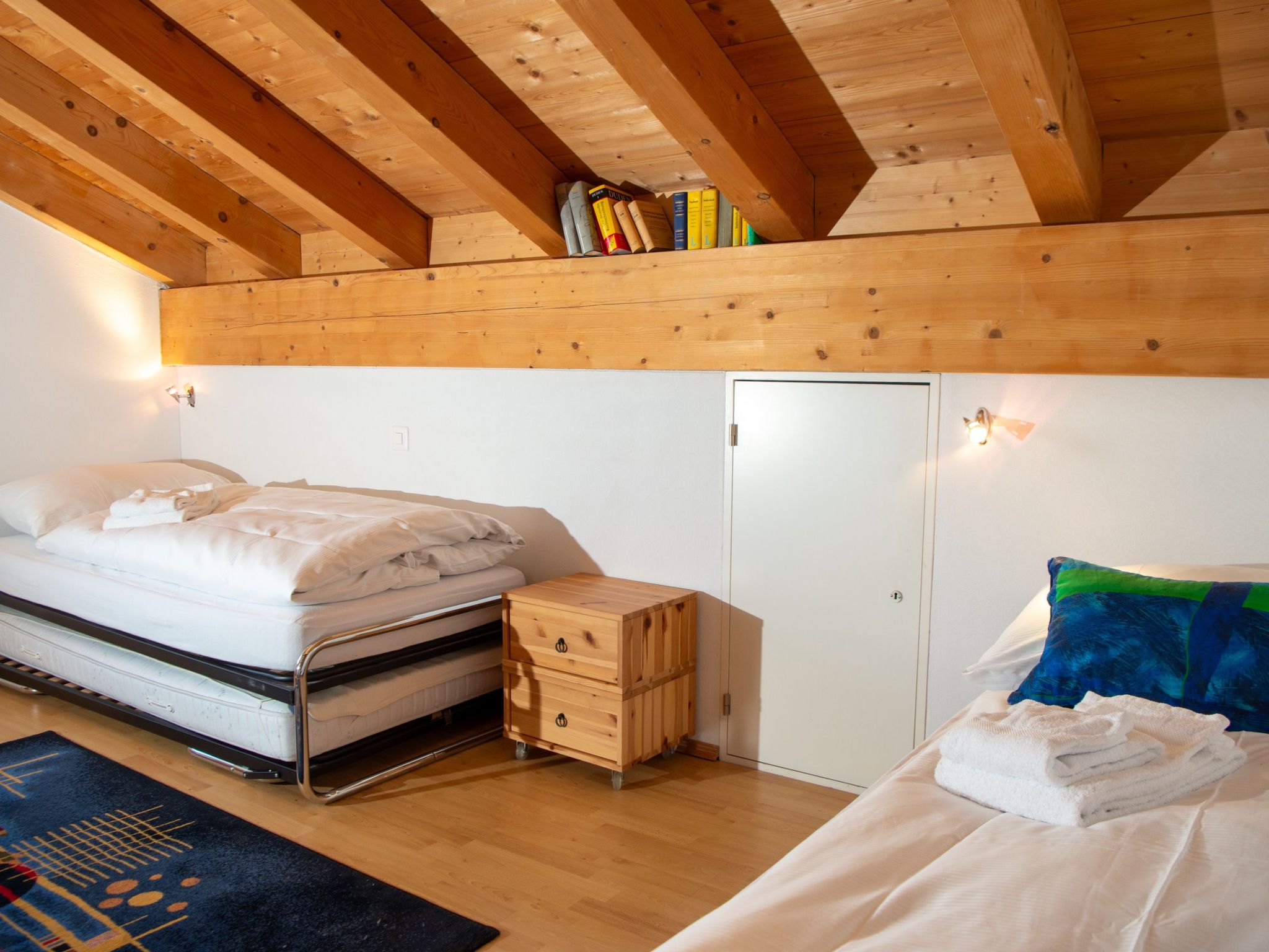 A bedroom with a bed, a bedside table, a wardrobe, and a shelf with books.