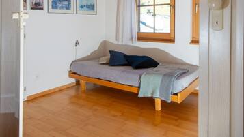 A small, cozy room with a single bed, a window with curtains, and a few framed pictures on the wall.