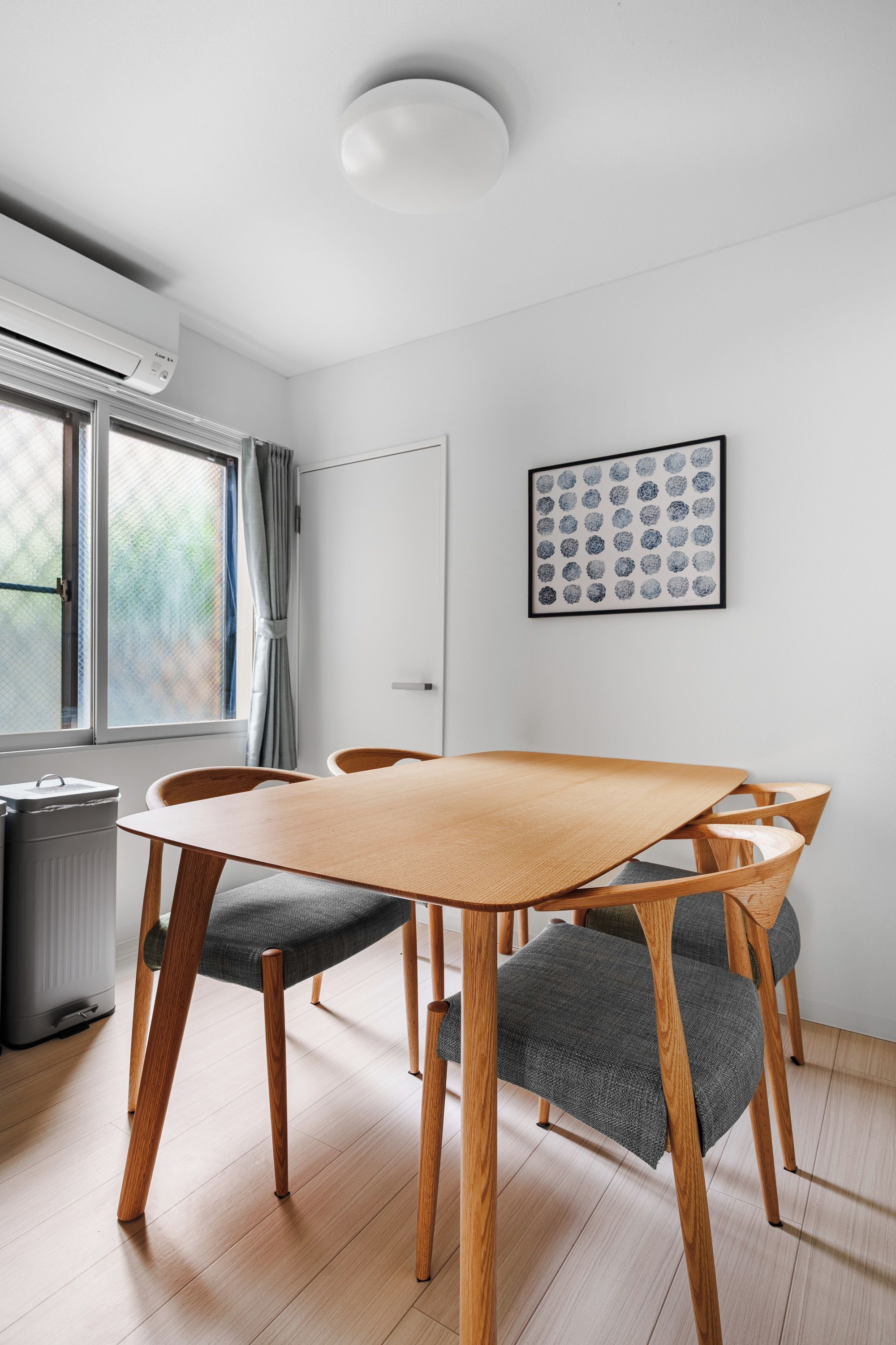A modern dining area with a wooden table and chairs, a radiator, a window with curtains, and a framed artwork on the wall.