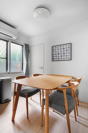 A modern dining area with a wooden table and chairs, a radiator, a window with curtains, and a framed artwork on the wall. - Billboard 101 (Sapporo)