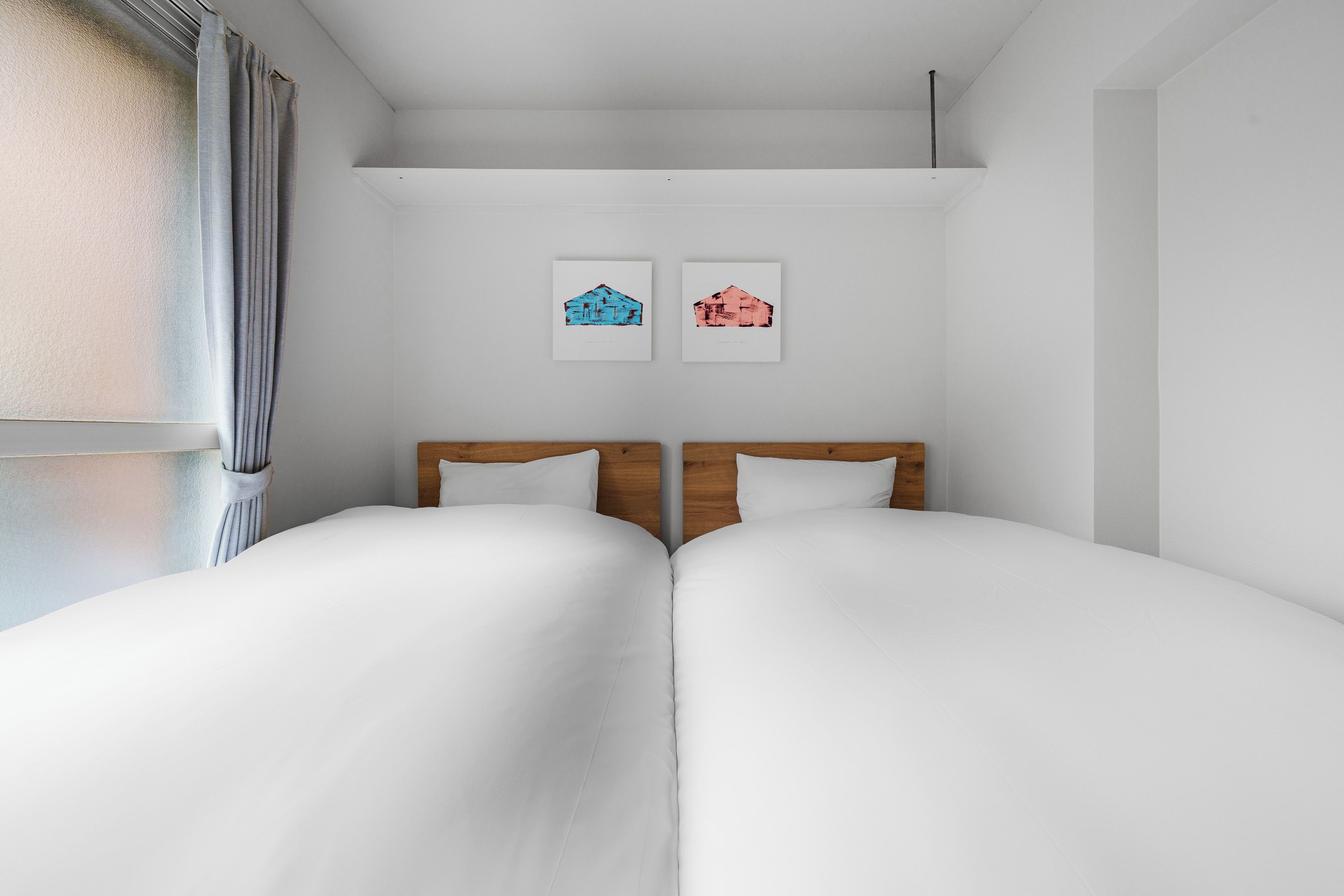 Cama doble con cabecera de madera, ropa de cama blanca y dos cuadros en la pared.