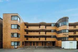 A multi-story building with a brick facade, multiple balconies, and a parking area in front. - Billboard 101 (Sapporo)
