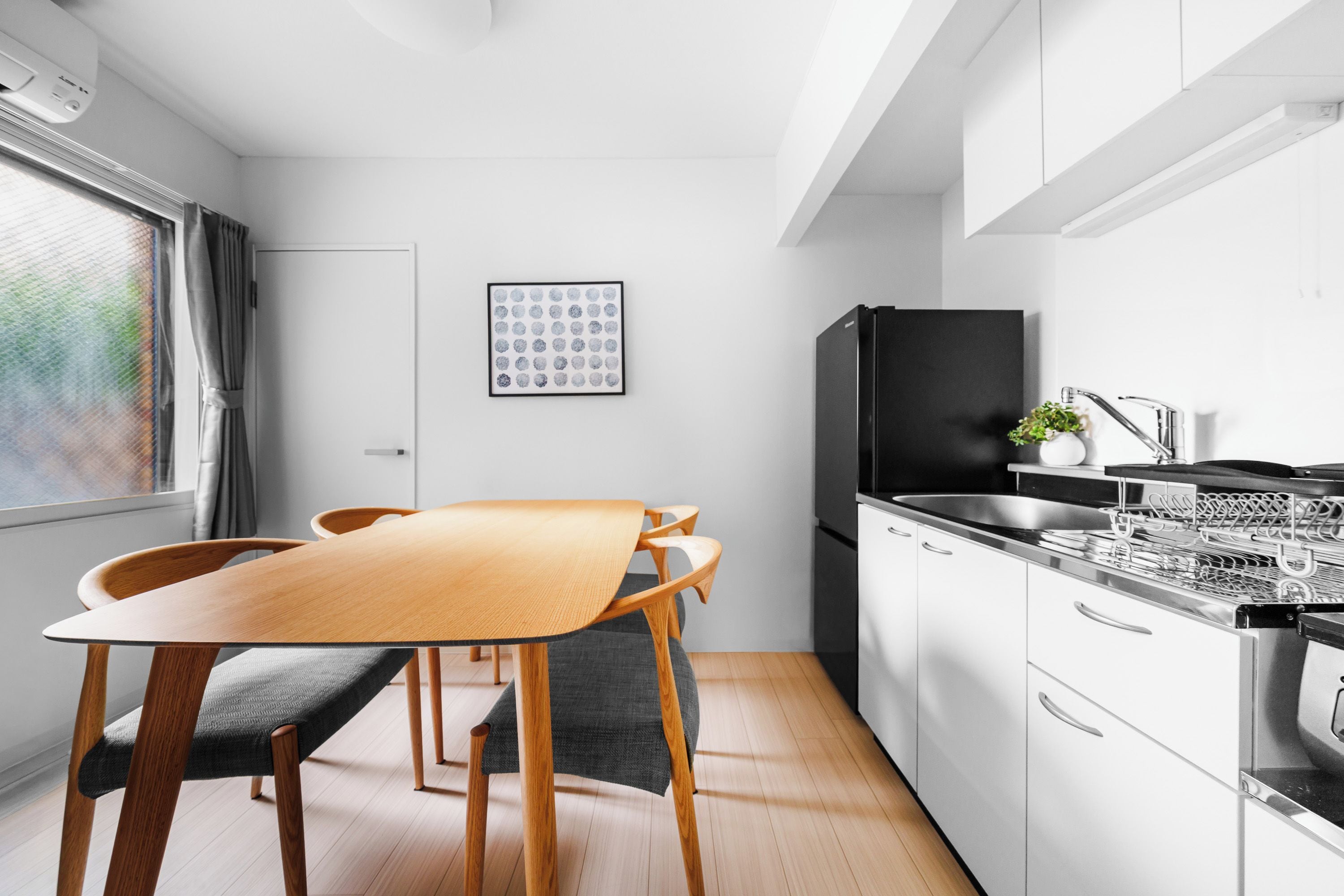 A modern kitchen with white cabinets, a black refrigerator, and a dining area with a wooden table and chairs.