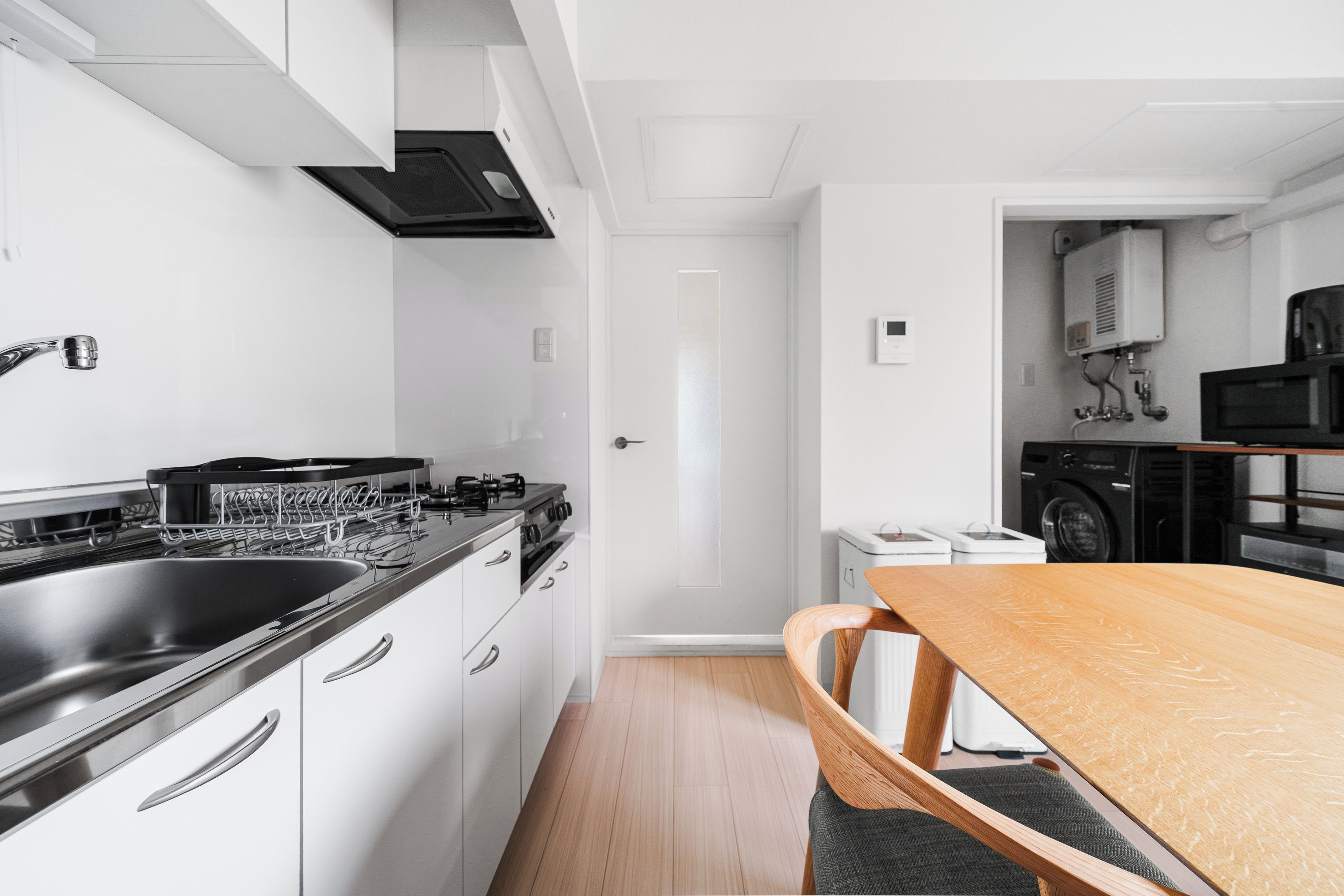 A modern kitchen with white cabinetry, a stainless steel sink, and a wooden dining table.